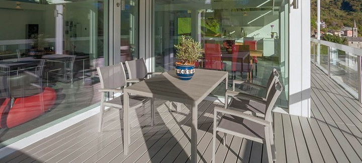 Überdachte Terrasse mit grauem Holzboden, modernem Esstisch-Set und Blick in den offenen Wohnbereich.
