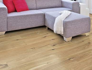 Im Wohnzimmer ist Parkett in Langdielen-Optik verlegt. Dazu passt ein Ecksofa mit bunten Kissen.