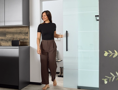 Frau schiebt eine Glastür auf und betritt die Küche.