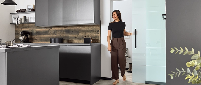 Frau schiebt eine Glastür auf und betritt die Küche.