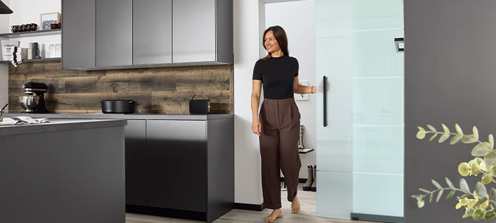 Frau schiebt eine Glastür auf und betritt die Küche.