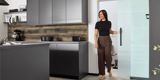 Frau schiebt eine Glastür auf und betritt die Küche.